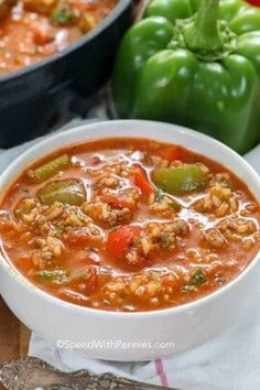 a white bowl filled with soup next to two green peppers and a spoon on a table