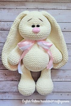 a white stuffed animal with a pink ribbon around its neck sitting on a wooden surface