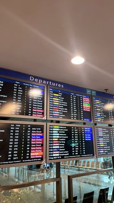 an airport departure board with multiple times displayed on it's sides and people seated at tables in the background