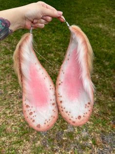 two pink and white furry animal tails being held by a person's hand in the grass