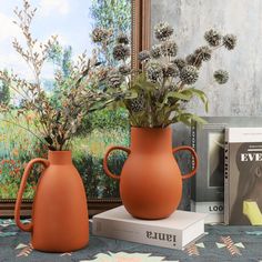 two vases with flowers in them sitting on a table next to books and magazines