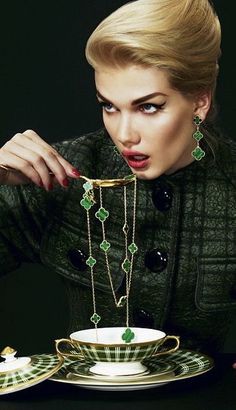 a woman is holding a tea cup and saucer with green jewels on it, while looking at the camera