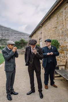 three men standing next to each other in front of a stone building with a bench