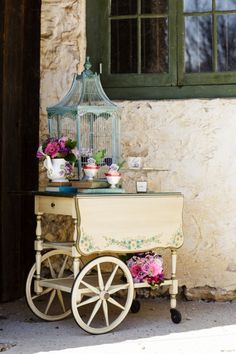 a bird cage sitting on top of a wooden cart next to a building with flowers