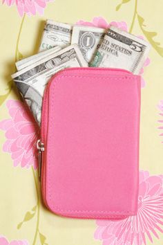 a pink wallet with money sticking out of it sitting on top of a flowered wall