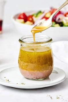 a spoon pouring dressing into a glass jar on a white plate with salad in the background