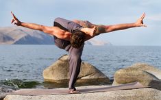 a man doing yoga on top of a rock by the water with his arms stretched out