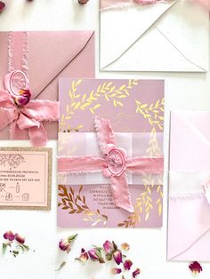 pink and gold wedding stationery with flowers on the bottom right hand corner, ribbon tied around it