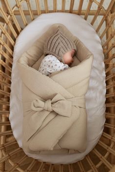 a baby wrapped in a blanket is laying in a wicker basket with a white pillow