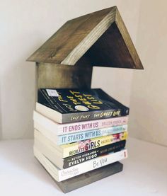 a stack of books sitting on top of each other in a small wooden house shape