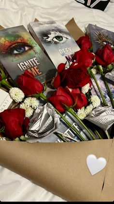 a bouquet of roses and books in a box on top of a white bed sheet