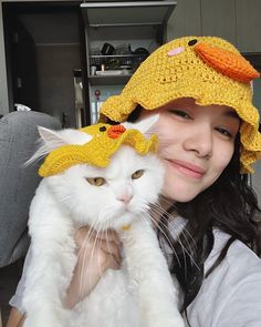 a woman holding a white cat wearing a yellow hat