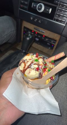 a hand holding a glass bowl filled with ice cream and candy on top of a napkin