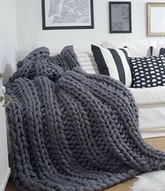 a living room with white walls and black and white pillows on the floor, blankets are draped over the couch