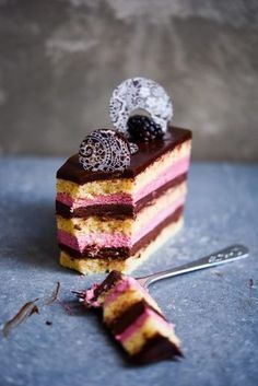 a piece of cake with chocolate and raspberry toppings on top, next to a fork