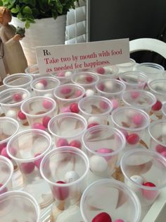 plastic cups filled with pink and white candy on top of a table next to potted plants