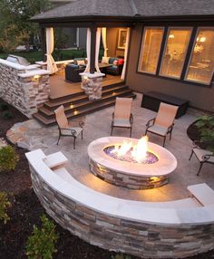 an outdoor fire pit in the middle of a patio with chairs and tables around it