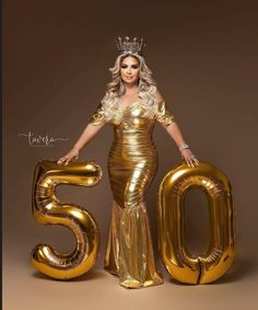 a woman in a gold dress and crown standing next to the number 50 with balloons