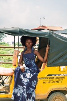 a woman in a blue and white dress sitting on the back of a yellow vehicle