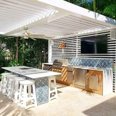 an outdoor kitchen with grill and bar stools under a pergolated awning