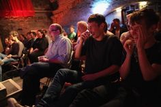 a group of people sitting next to each other in front of a brick wall with red curtains