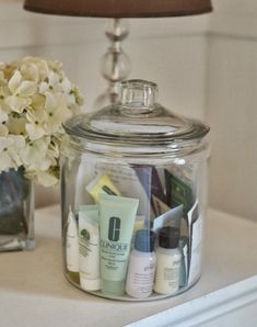 a glass jar with some skin care products in it and a lamp next to it