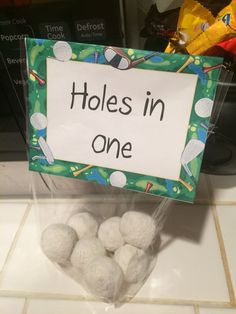 a bag filled with white balls sitting on top of a counter next to a sign that says holes in one