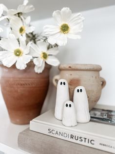 two white ghost figurines sitting on top of a book next to a potted plant