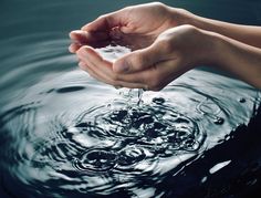 a person's hand holding water in the middle of a body of water with ripples