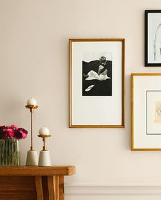 three framed pictures hang on the wall above a table with vases and flowers in front of it