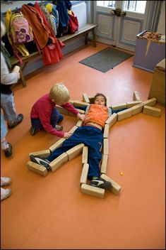 two children are playing on the floor in a room with orange floors and wooden furniture