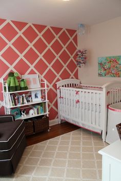 a baby's room decorated in pink, white and green with geometric wallpaper