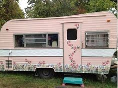 an old pink camper with flowers painted on it's side parked in the grass