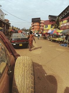 a man walking down a dirt road next to parked cars and people on the street