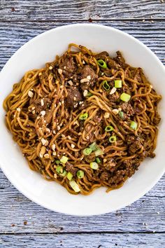 a white bowl filled with noodles and meat on top of a wooden table next to chopsticks