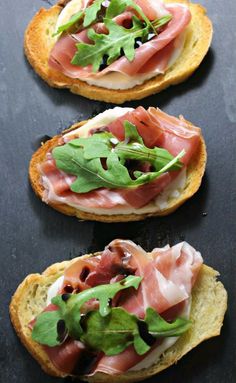 three slices of bread with meat and greens on top, sitting on a black surface