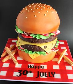 a birthday cake made to look like a hamburger and fries on a red checkered tablecloth