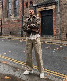 a man standing in front of an old brick building with his arms crossed and looking off to the side