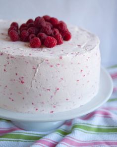 a white cake with raspberries on top sitting on a plate next to a towel