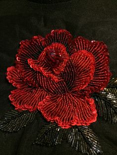 a red flower with sequins on it sitting on top of a black shirt