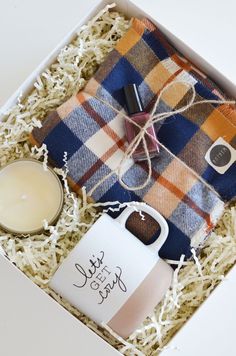 an open box containing a candle, plaid blanket and tea