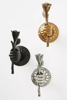 three different types of decorative wall hooks on a white wall, one holding a rose and the other pointing up