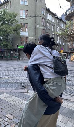 two people walking down the street with one carrying a child on his back and another carrying a backpack