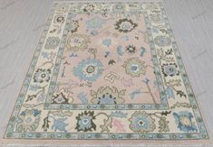 This exquisite hand-knotted Oushak wool rug boasts a serene pastel palette, predominantly featuring soft pinks, blues, and earthy greens. Its intricate floral and geometric motifs, typical of traditional Oushak designs, offer a blend of modern and classic elements. The rug's central field showcases large, abstract floral patterns in shades of pale pink and sky blue, accompanied by olive green accents. These motifs are harmoniously framed by a wide border adorned with complementary floral designs Traditional Floral Design, Earthy Greens, Custom Area Rugs, Area Rug For Living Room, Pastel Palette, Geometric Motifs, Rug For Living Room, Green Accents, Large Abstract