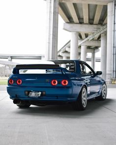 the back end of a blue sports car parked in front of an overpassed building