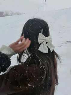 a woman standing in the snow with her hair tied back and wearing a white bow