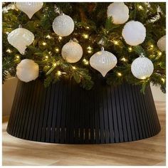 a christmas tree with white ornaments and lights on it's branches in a black container