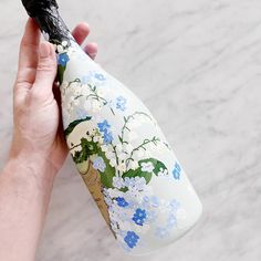 a hand holding a white and blue vase with flowers on it