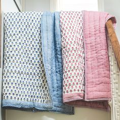 four different colored blankets hanging on a clothes line next to a window with a wooden hanger