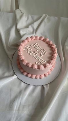 a pink birthday cake sitting on top of a white tablecloth covered sheeted bed